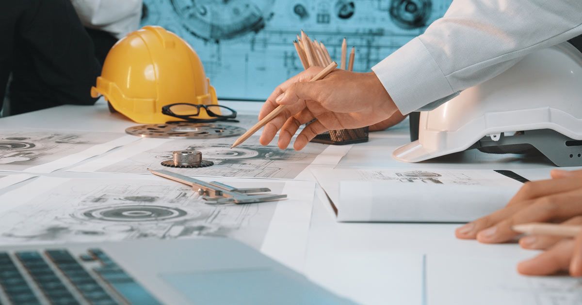 Websites for Engineers by Solution Web Designs, showing Engineers reviewing blueprints, using pencils and tools, next to hard hats, glasses, and a laptop.