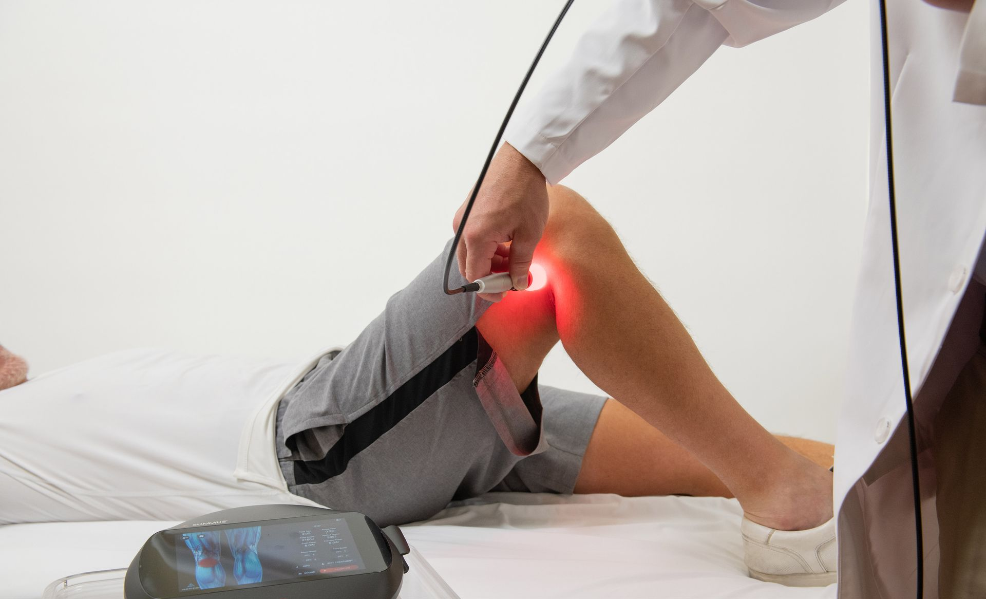 Person doing physical therapy with a red-lit knee treatment device on a treatment table