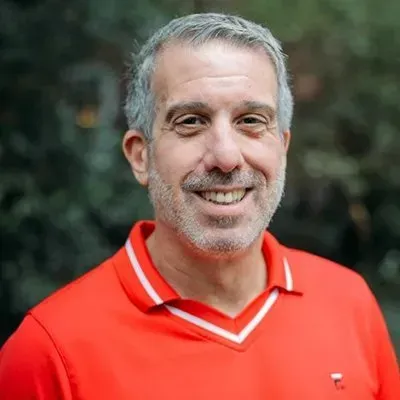 Smiling man in a red collared shirt outdoors with a blurred green background
