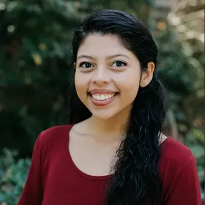 Smiling woman in a red top standing outdoors against a leafy background
