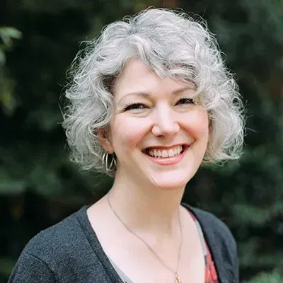 Smiling person with short curly gray hair wearing a dark cardigan outdoors