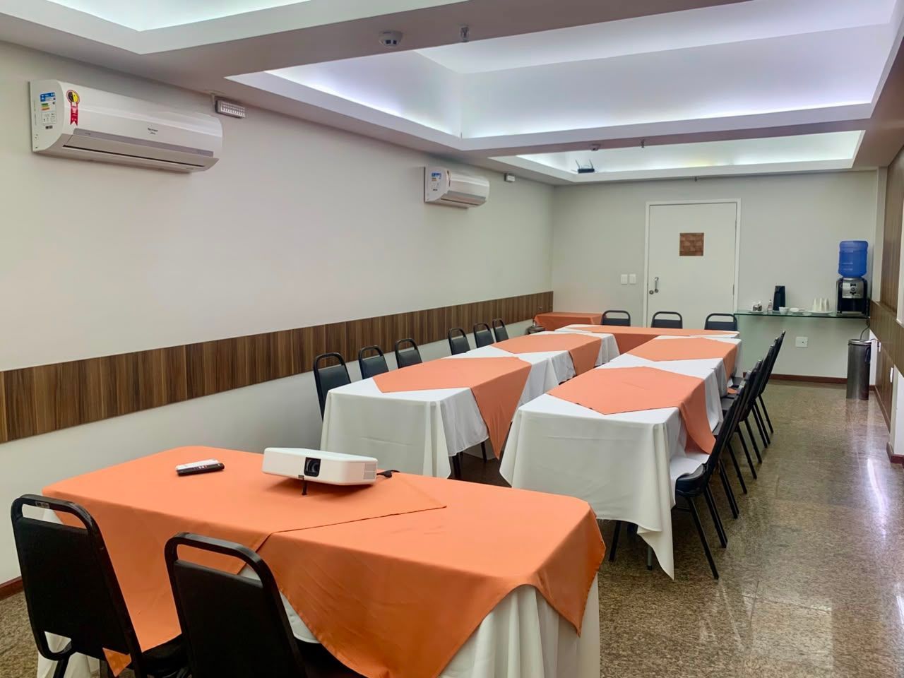 Buffet de café da manhã com diversos itens alimentares: pães, bolos, frutas e pratos quentes, em um refeitório.