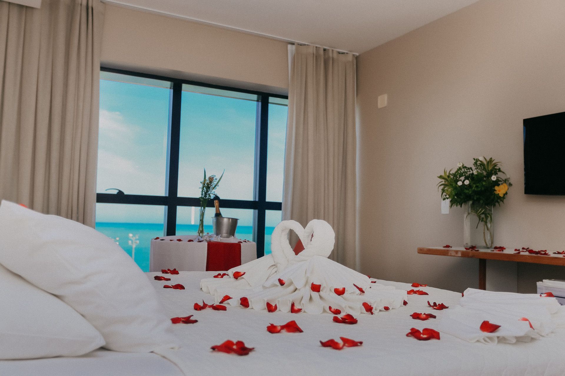 Quarto de hotel romântico com arte em forma de cisne feita com toalhas, pétalas de rosa e vista para o mar.