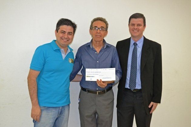 Três homens estão posando para uma foto e um homem está segurando um cheque