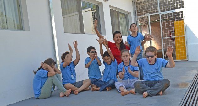 Um grupo de crianças está sentado no chão com os braços no ar