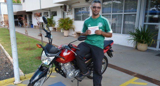 Um homem de camisa verde está sentado em uma motocicleta vermelha