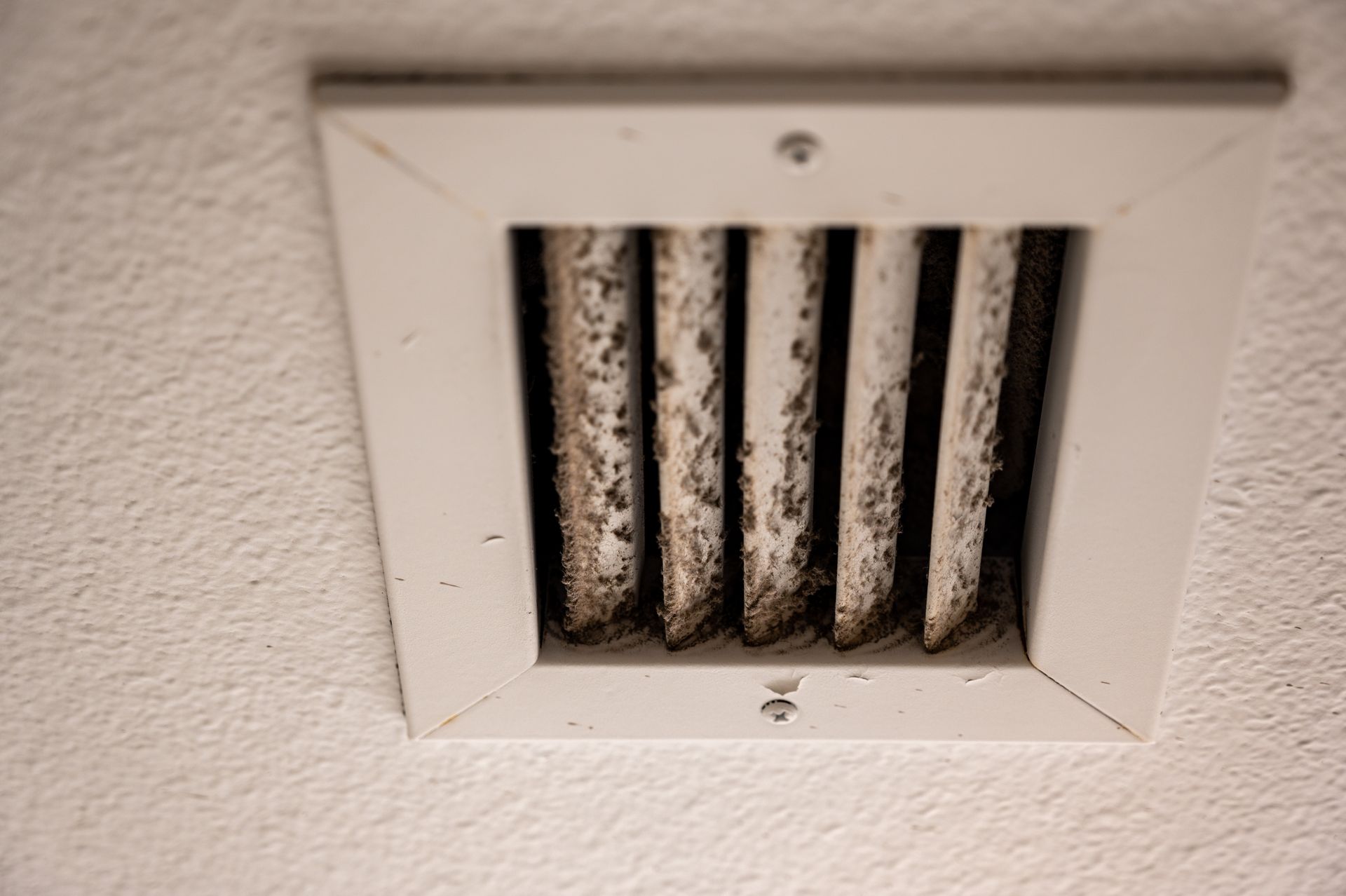 A close up of a dirty air vent on a wall.