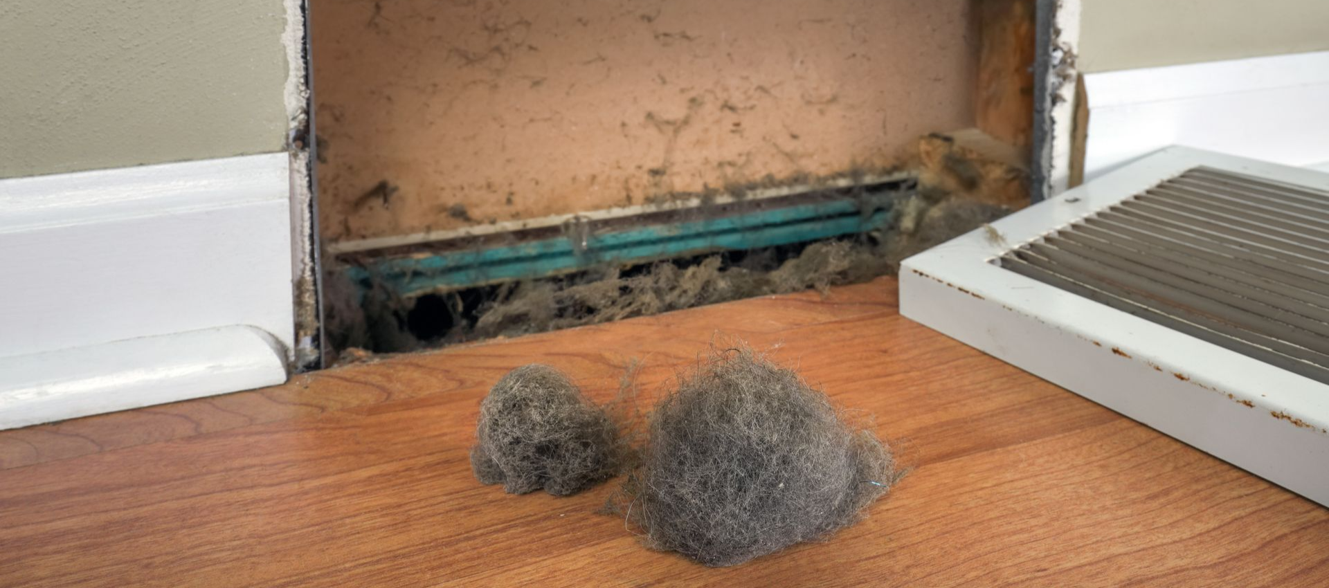 A dirty air vent with two clumps of collected dust and the vent cover next to it.