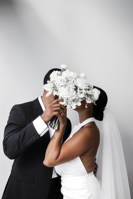 Black-and-white portrait of a couple standing close together, smiling against a plain backdrop.