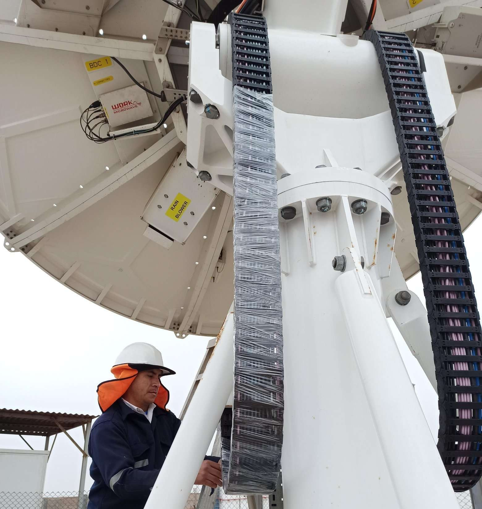 Worker with hardhat working at the base of a satellite antenna