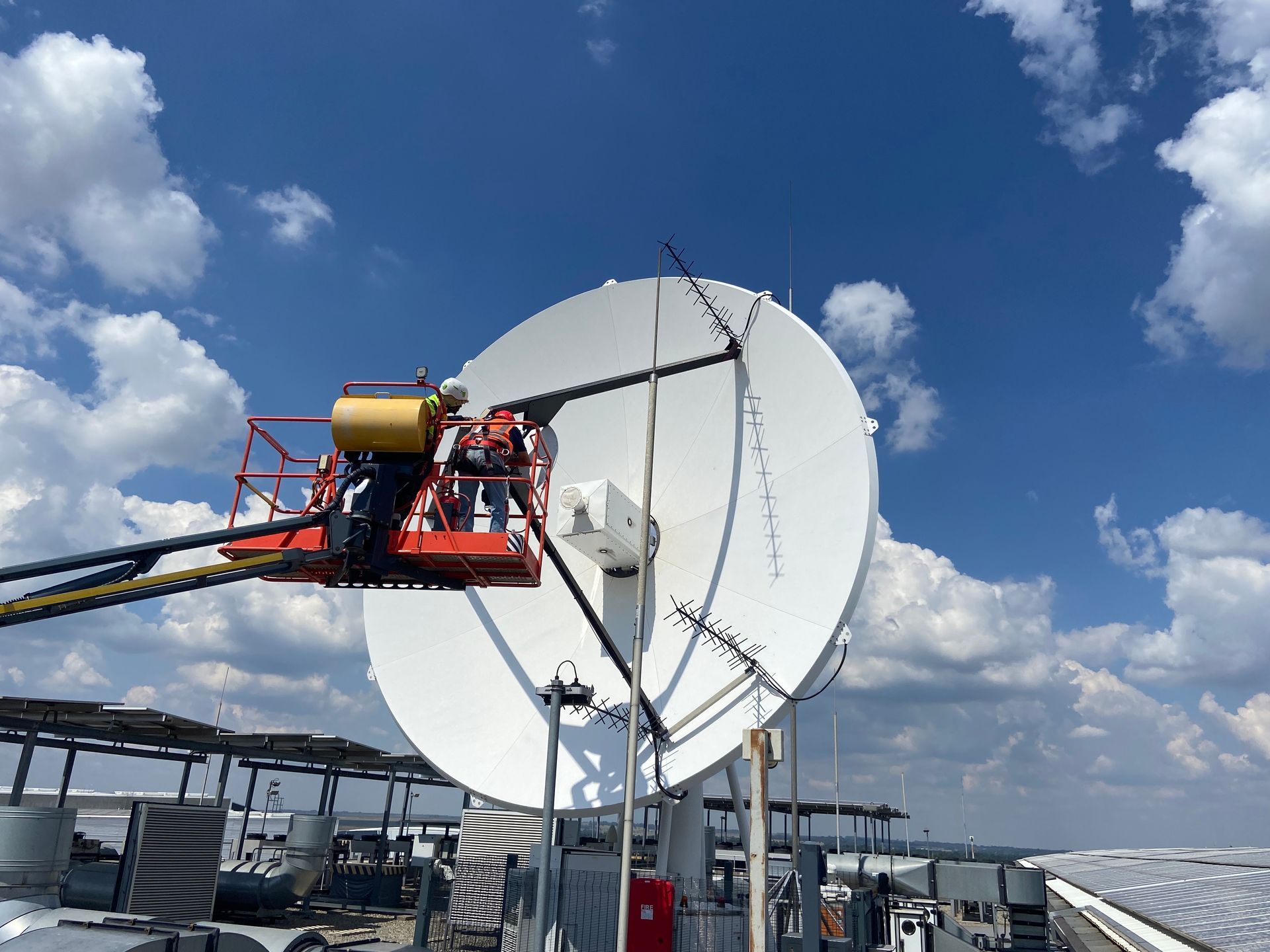 Two men in a cherry picker working on  satellite antenna dish. 
