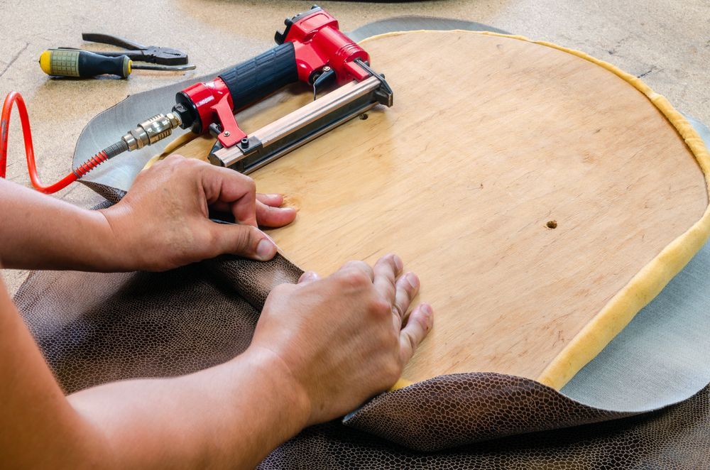 Person Using a Staple Gun to Attach Fabric to a Wooden Chair Seat — Atherton Decor Centre In Malanda, QLD