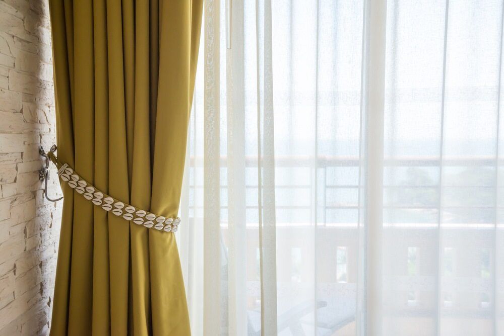 A Yellow Curtain is Hanging on a Window Next to a White Curtain — Atherton Decor Centre In Tablelands, QLD
