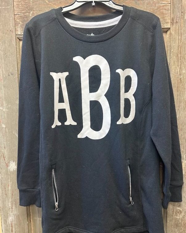 A black sweatshirt with a white monogram on it is hanging on a hanger.