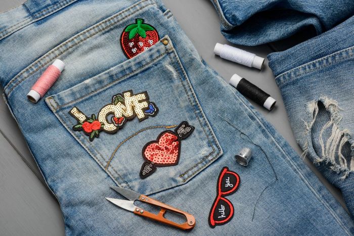 A pair of jeans with patches and sewing tools on it.