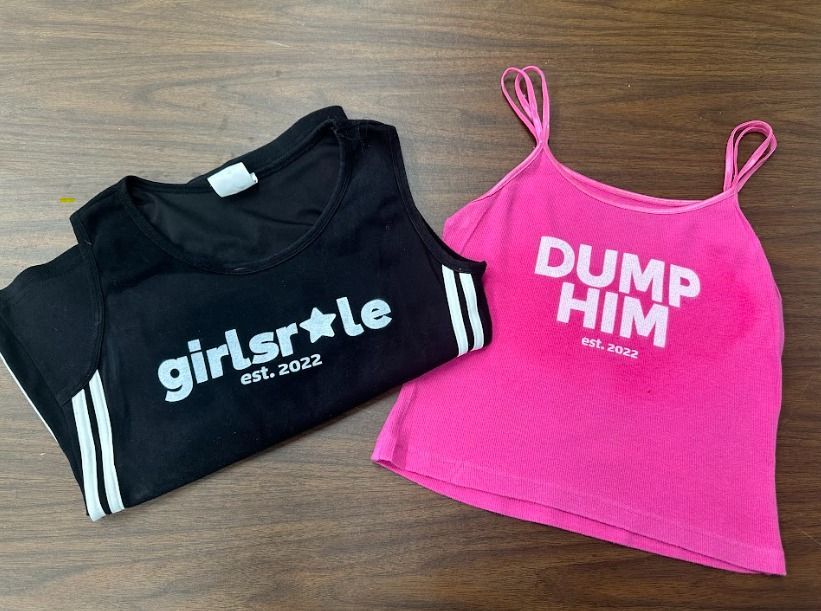 A black tank top and a pink tank top are sitting on a wooden table.