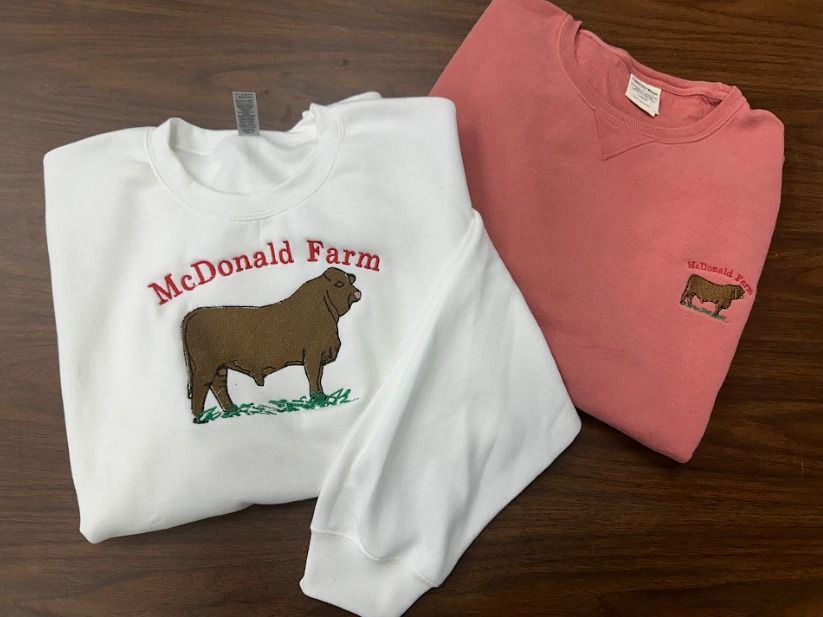 Two mcdonald farm sweatshirts are on a wooden table.