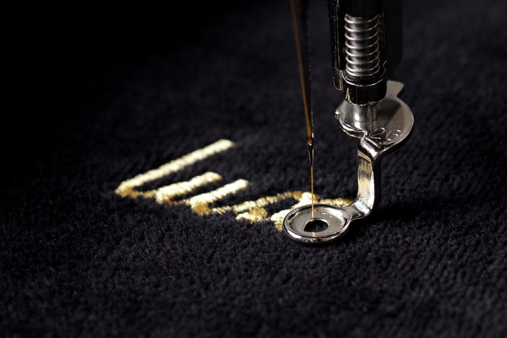 A close up of a sewing machine embroidery a word on a black cloth.