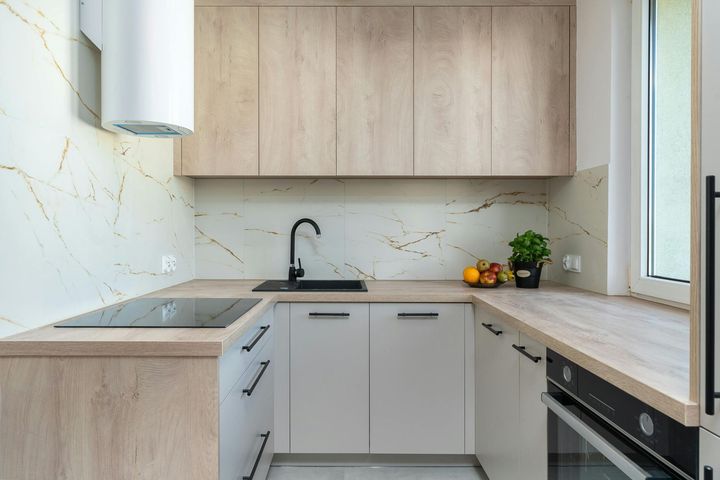 Modern minimalist kitchen with light wood cabinets, white counters, black fixtures, and a window by the sink