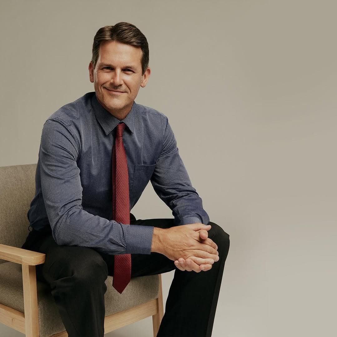A Man in a Blue Shirt and Red Tie is Sitting in a Chair — Bonanno's Menswear in Engadine, NSW