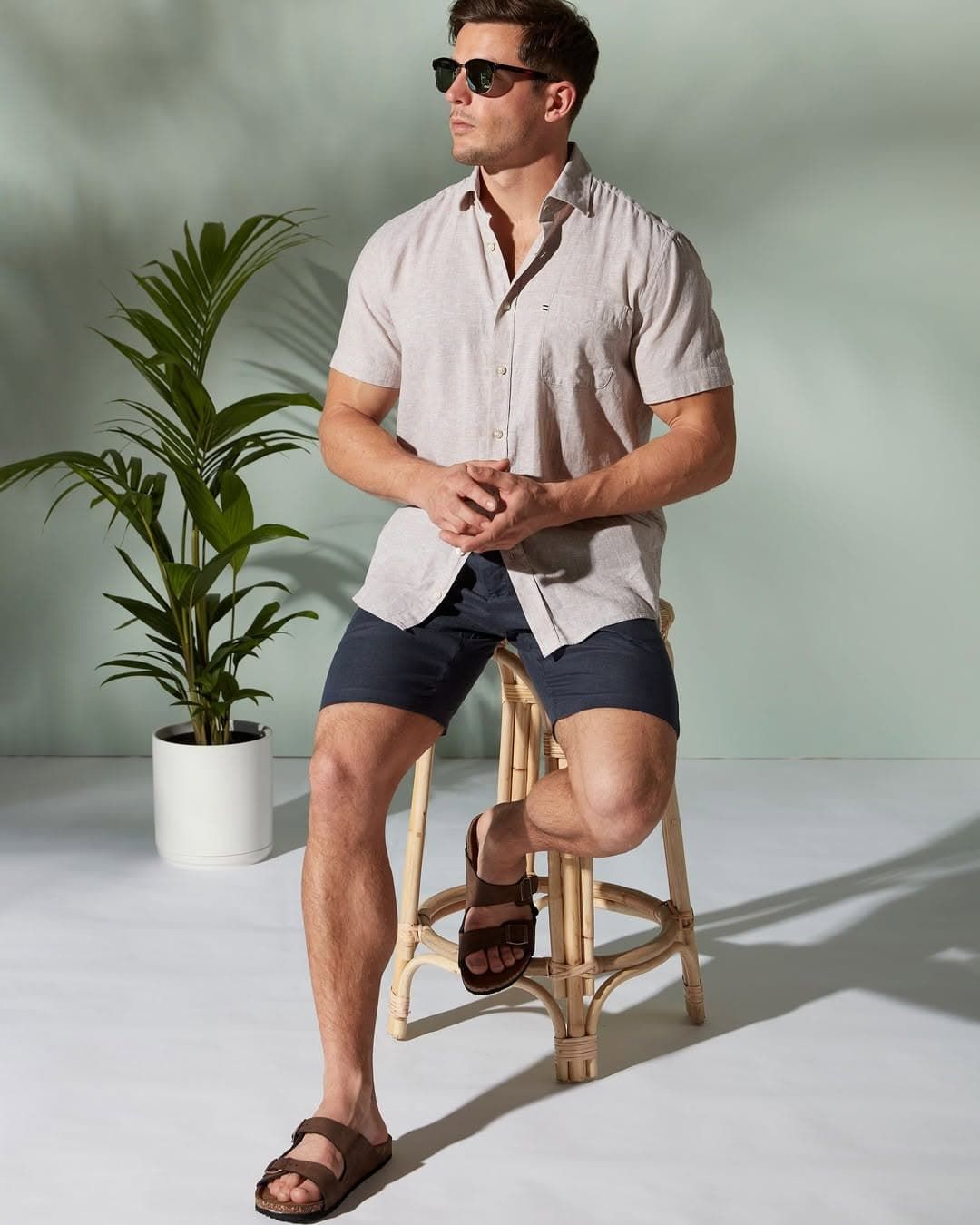 A Man Wearing Sunglasses and Shorts is Sitting on a Wooden Stool — Bonanno's Menswear in Shellharbour, NSW