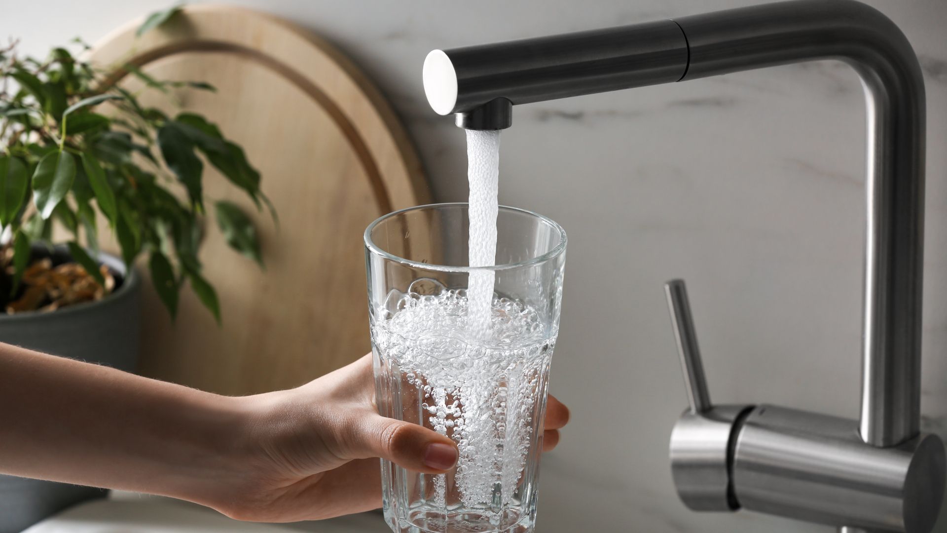 A person is pouring water into a glass from a faucet.