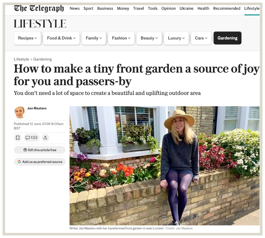 A person in a yellow hat, sweater, and boots sits in a garden chair, surrounded by potted plants and a wooden fence.