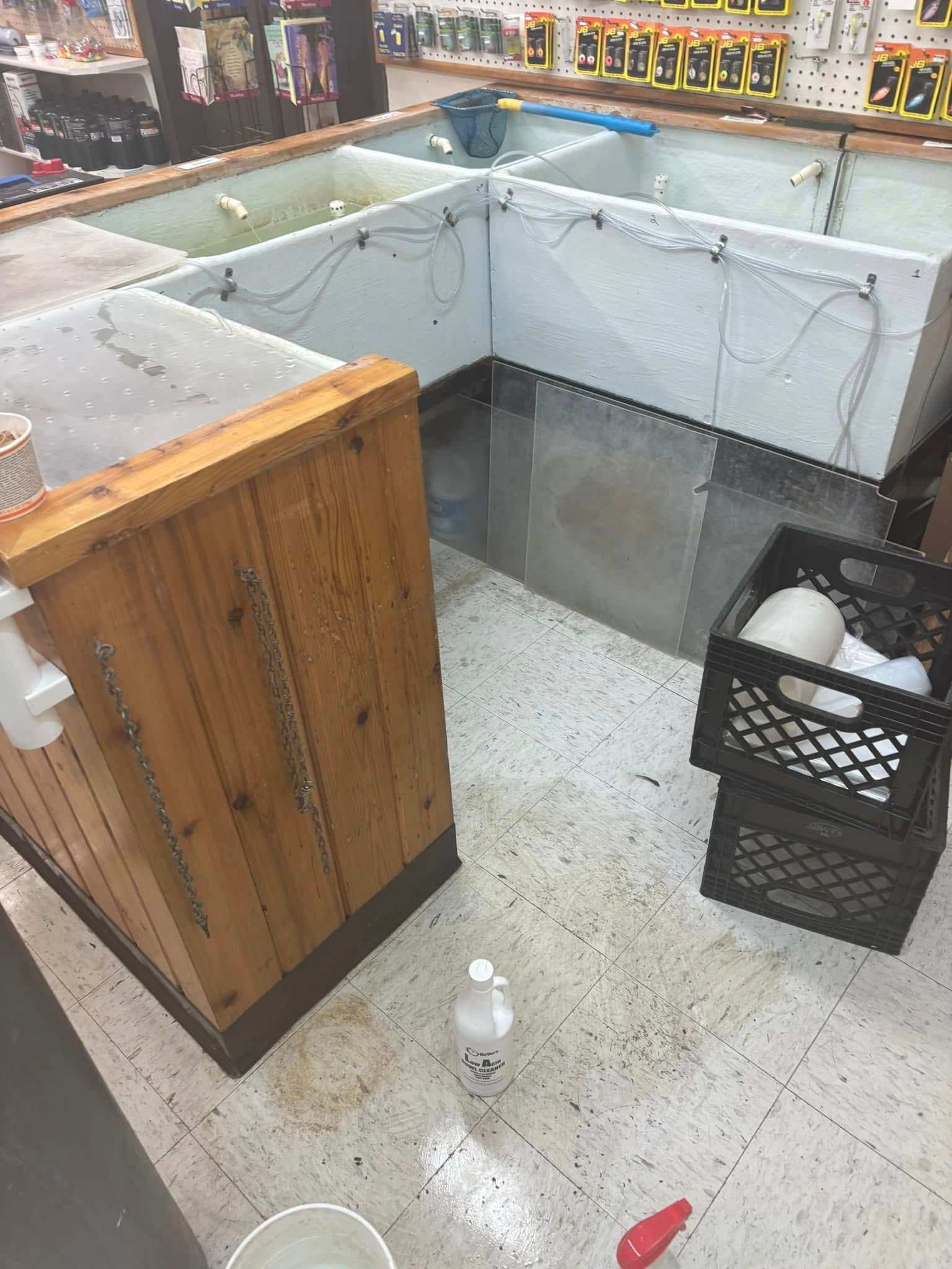 A view of a commercial fish tank setup in a retail shop with white tubs, a wooden counter, and plastic crates on the floor.