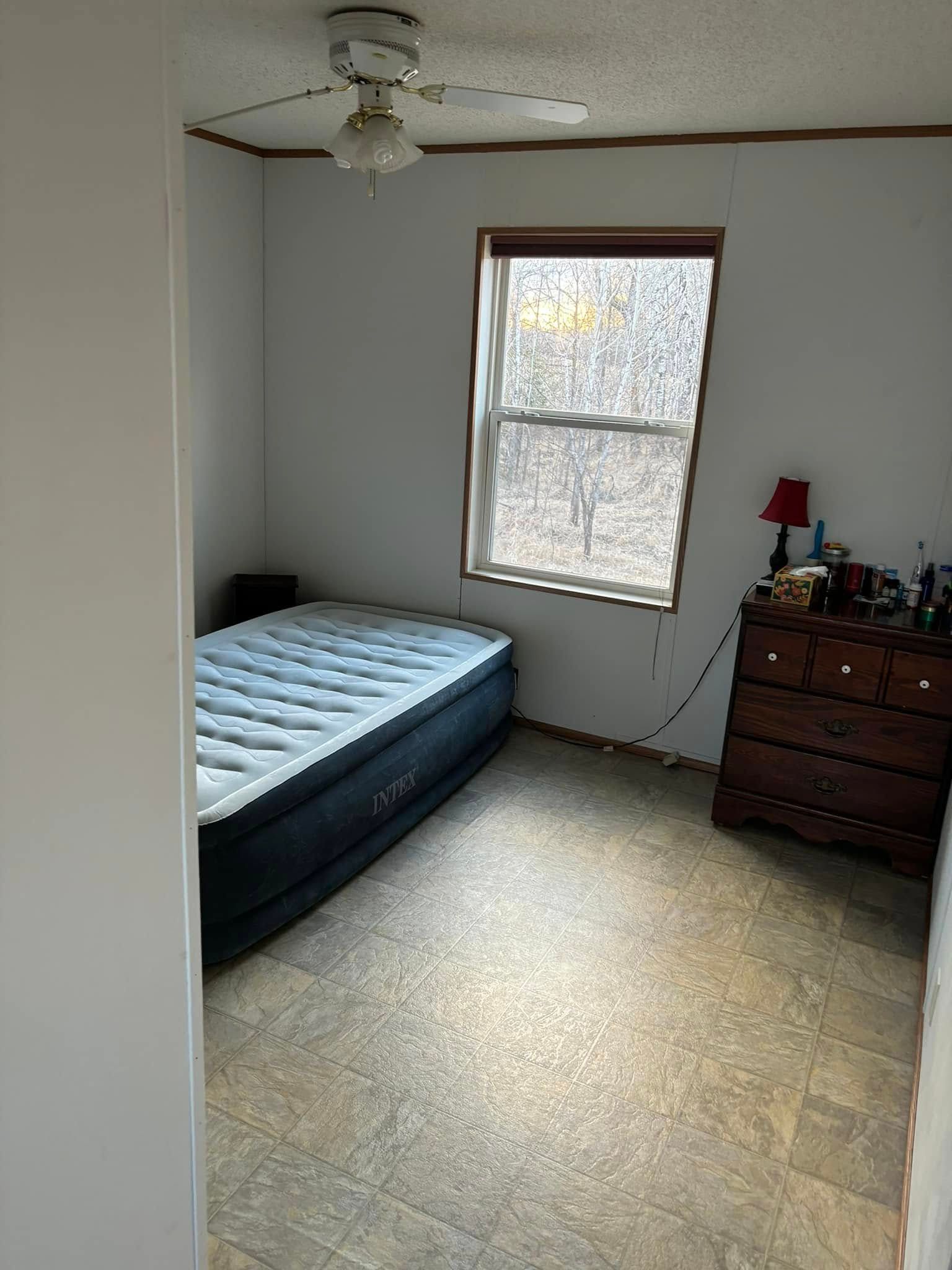 A small, sparsely furnished bedroom with a dark inflatable mattress, a wooden dresser, and a ceiling fan.