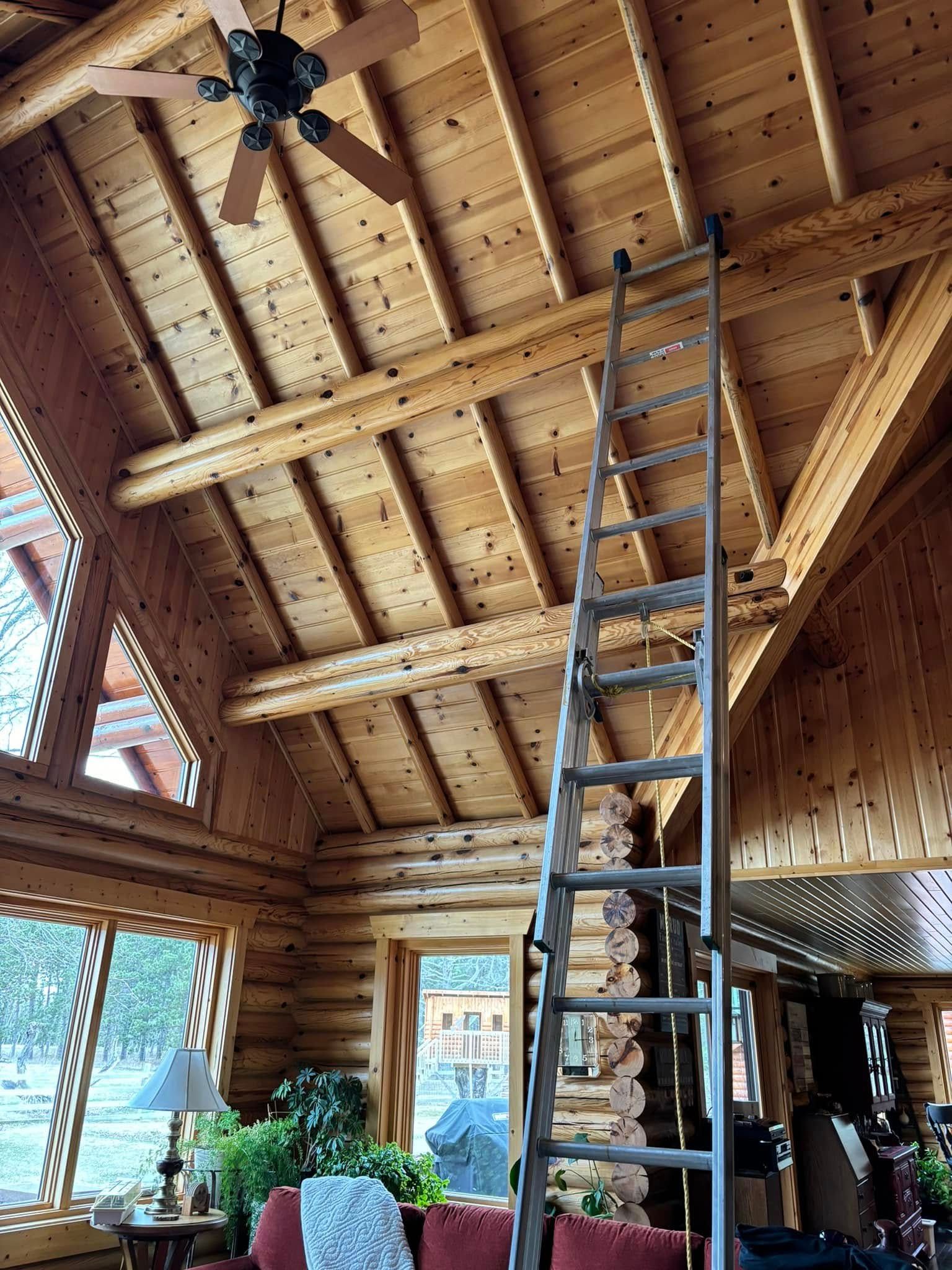 A tall extension ladder leans against the wooden beams of a high, vaulted log cabin ceiling.