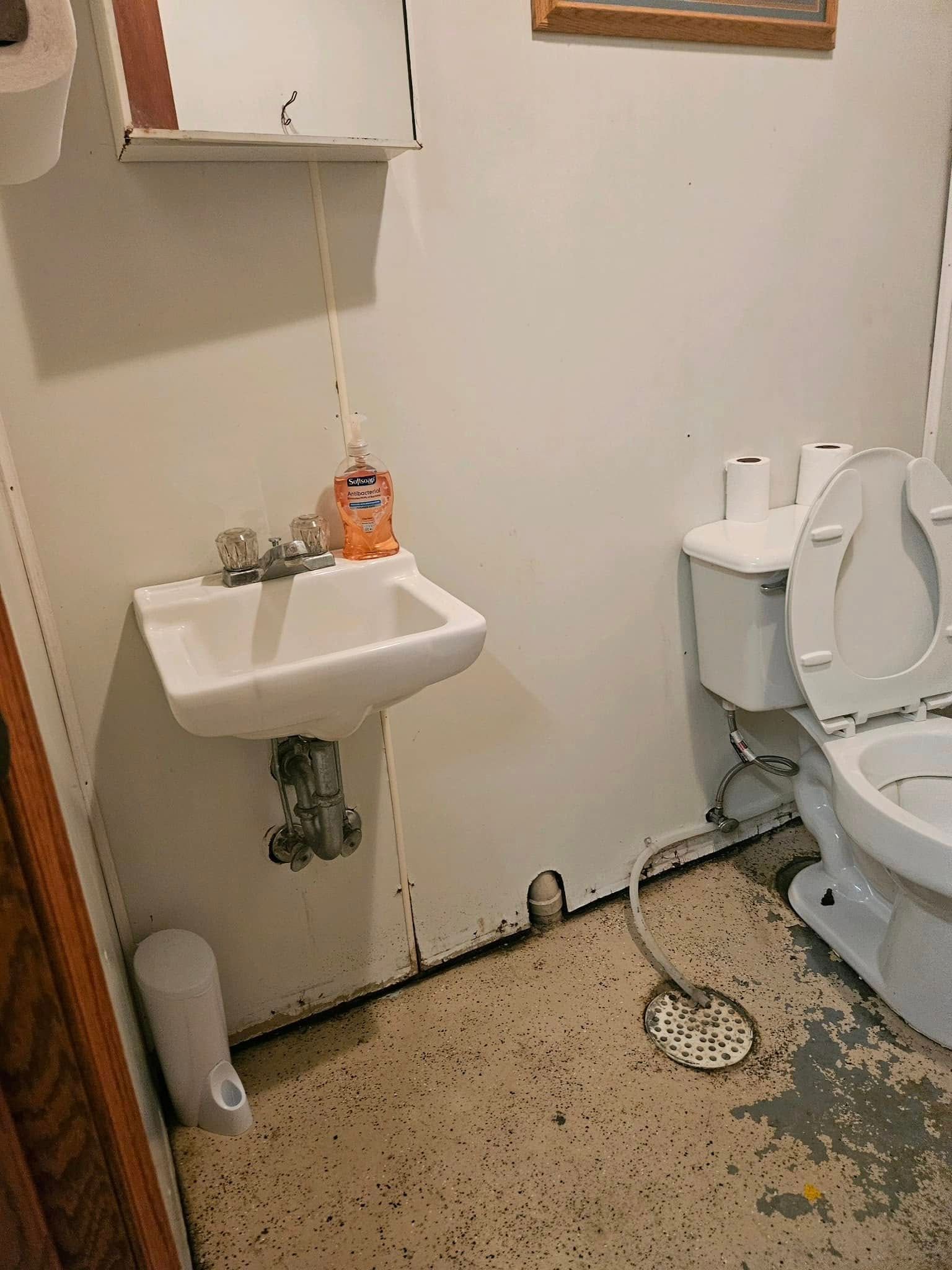 A small bathroom with a white wall-mounted sink, a toilet with the lid open, and concrete flooring.