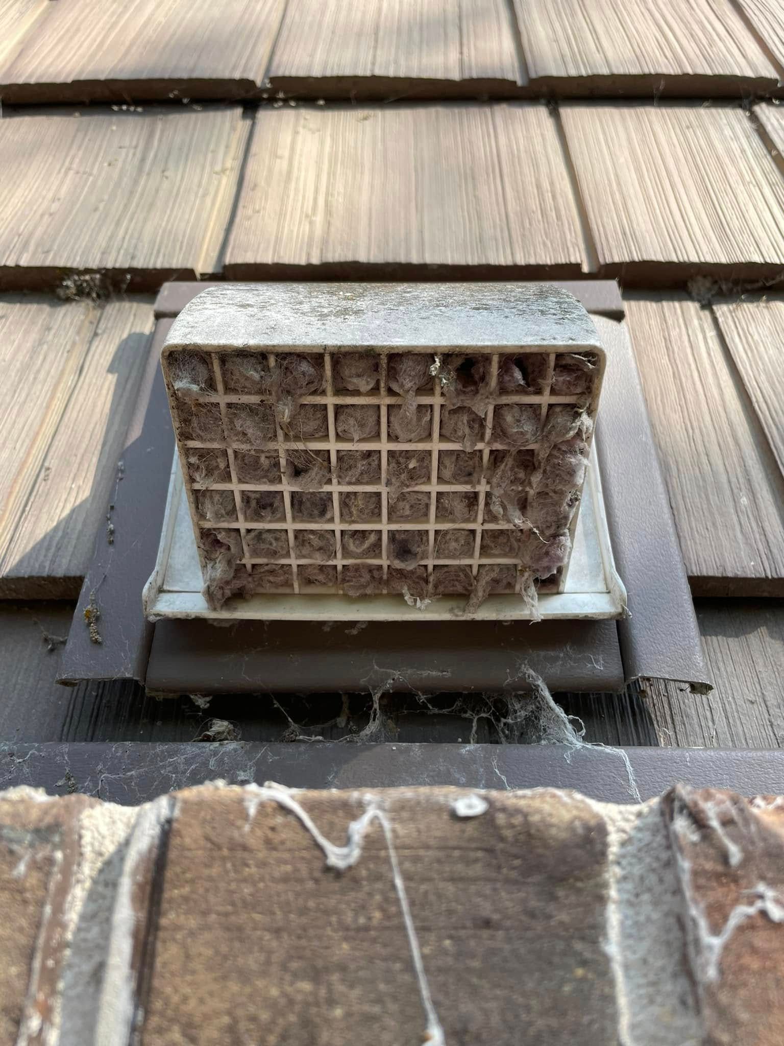 A white exterior vent cover on a brick wall, heavily clogged with lint or dust buildup.