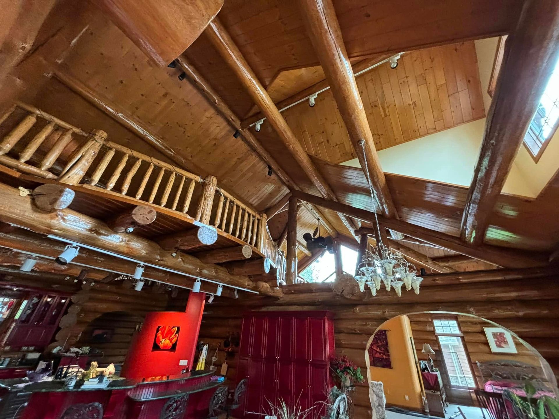 A rustic log cabin interior features high beamed ceilings, a wooden mezzanine balcony, and a vibrant red kitchen area.