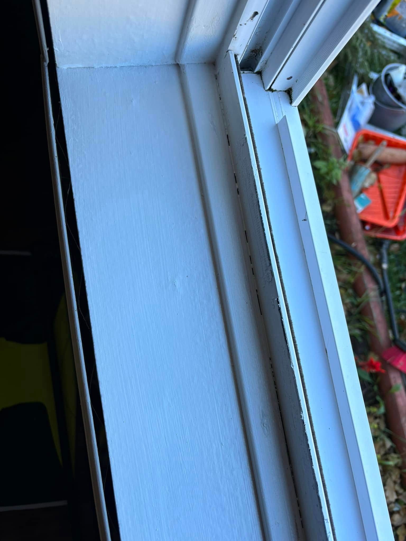 Close-up of a white painted window sill and frame with a glimpse of outdoor yard tools and greenery outside.