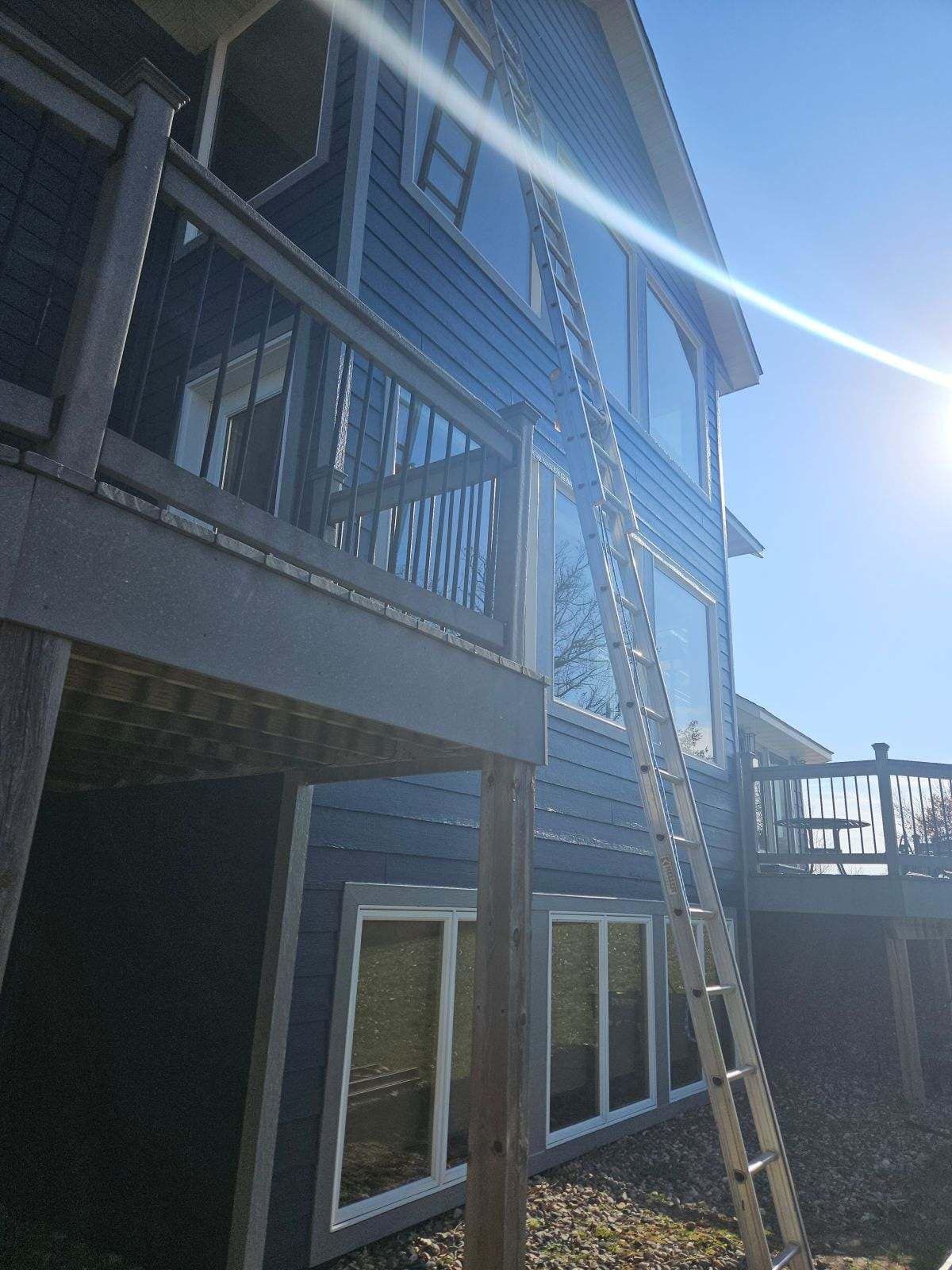 An extension ladder leaning against the blue-sided exterior of a house with a wooden deck.