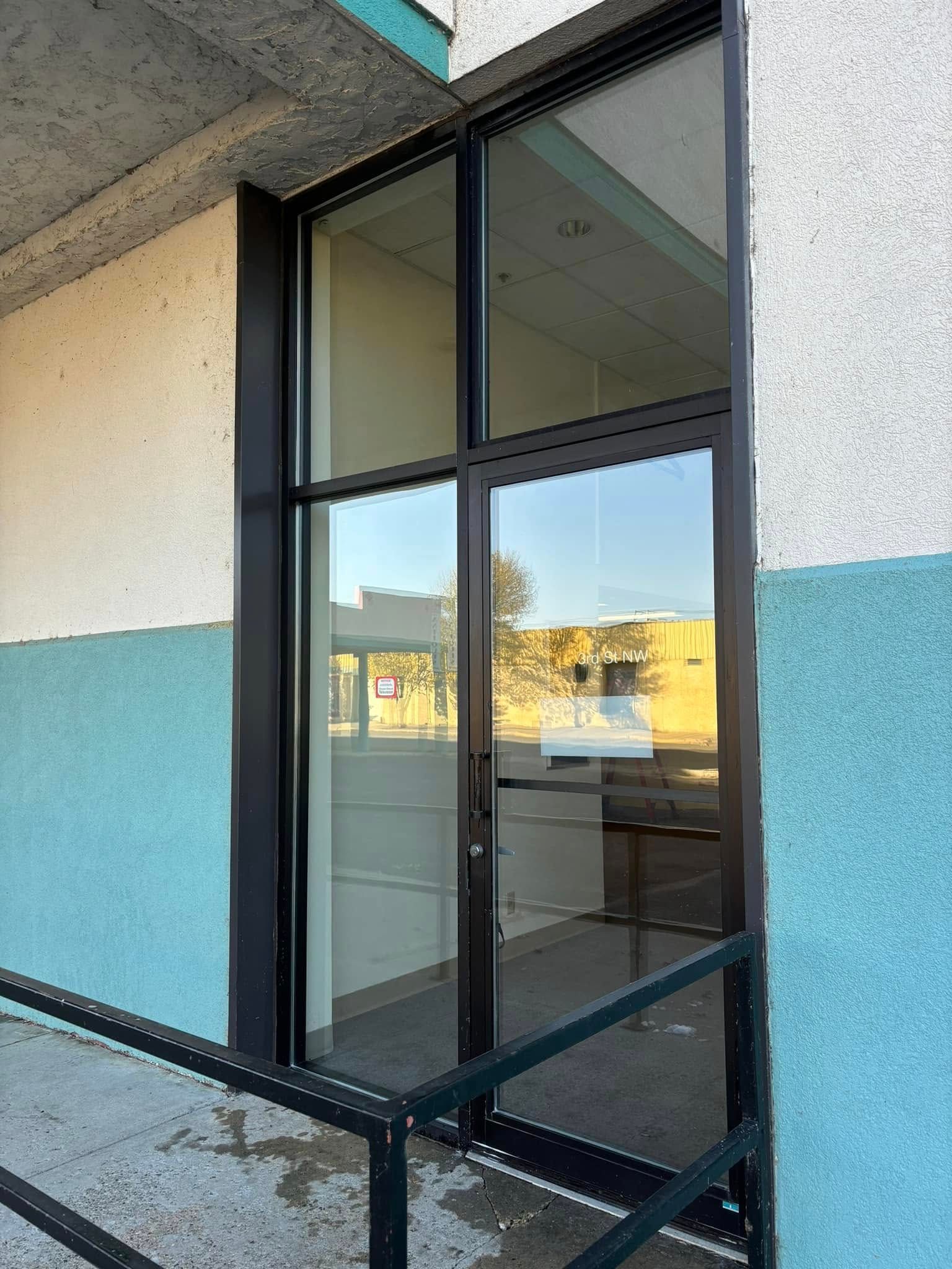 A storefront entrance with a dark metal-framed glass door, exterior stairs with black railings, and teal and cream walls.