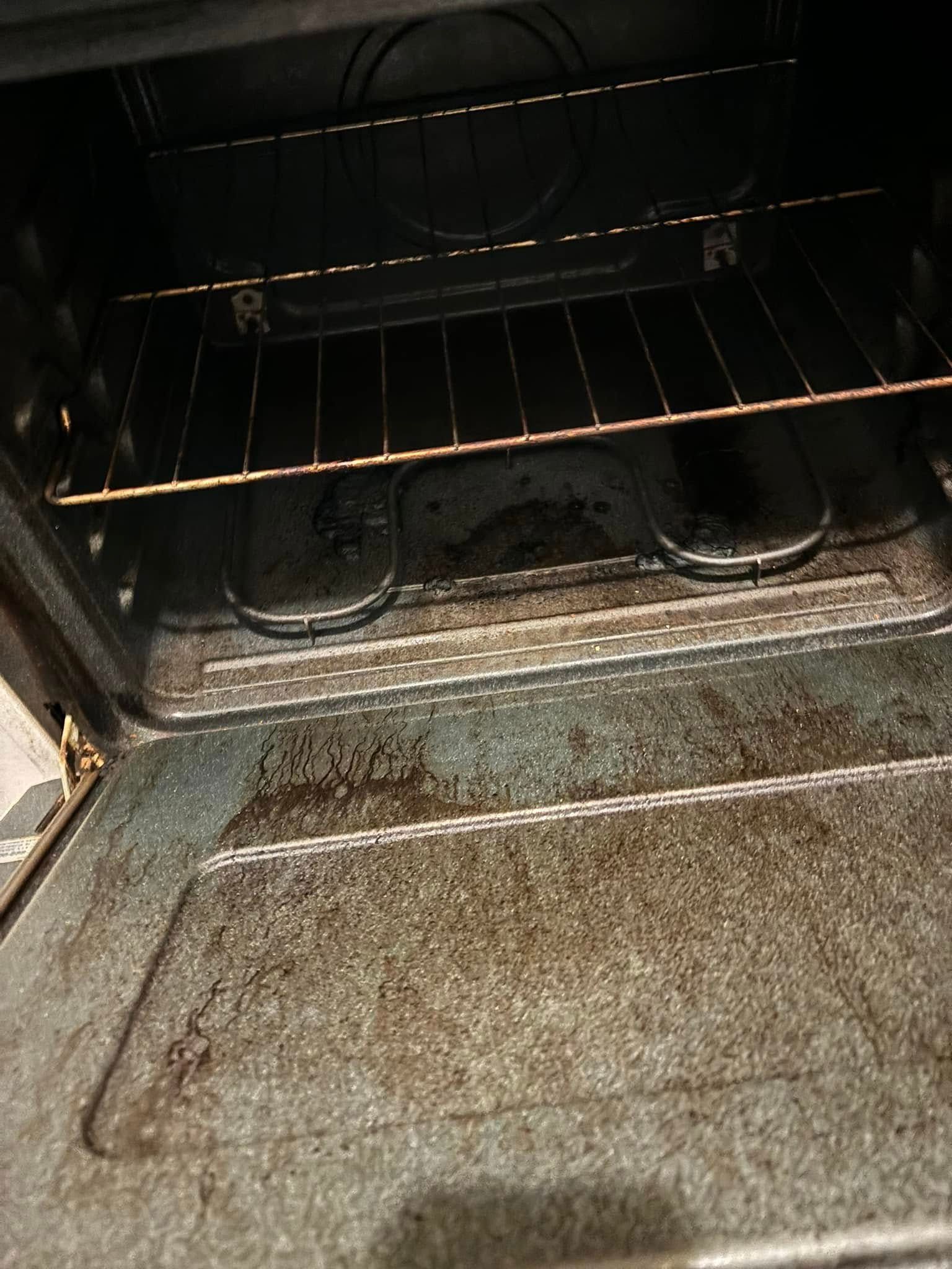 An open oven with a wire rack inside, showing significant grease buildup on the door and bottom interior surfaces.