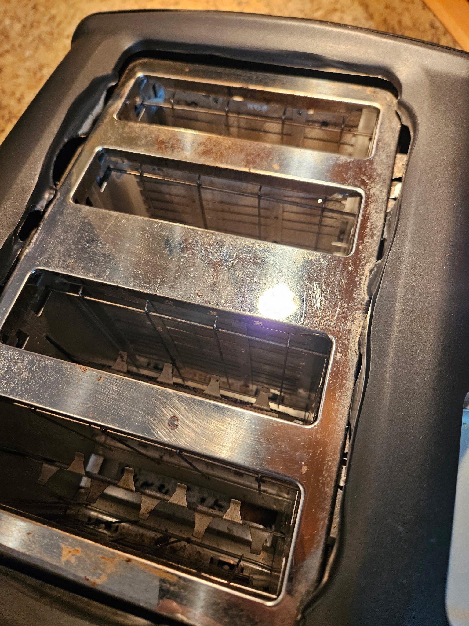 A top-down view of a four-slot black and chrome toaster with debris visible inside the slots.