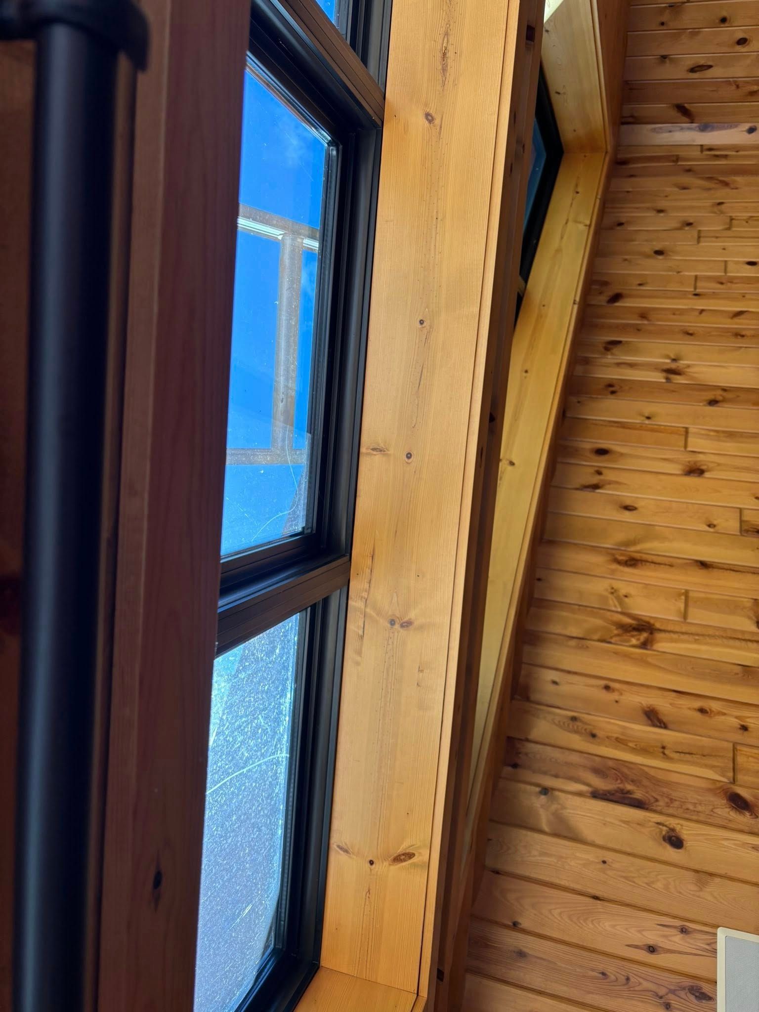 A close-up view of a black-framed window set into a wall of light-colored, tongue-and-groove wood planks.