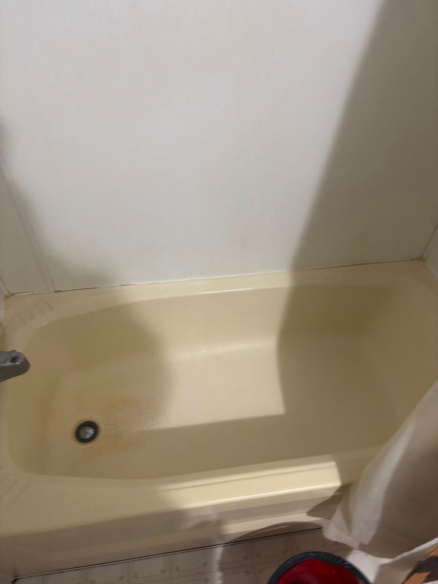 A cream-colored bathtub with a drain and a shower faucet, set against white walls.