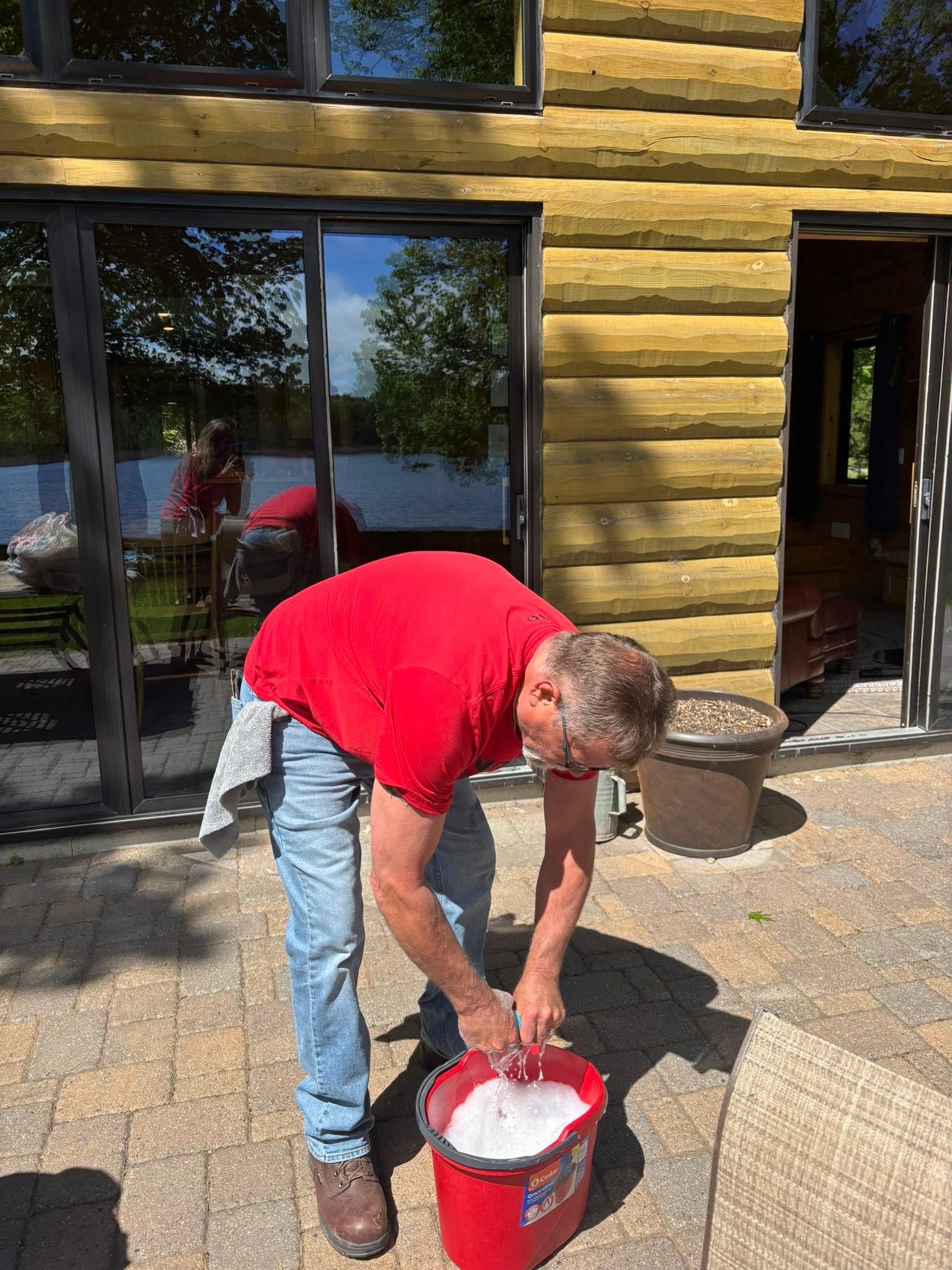 Man in red shirt washing windows outside a log cabin.