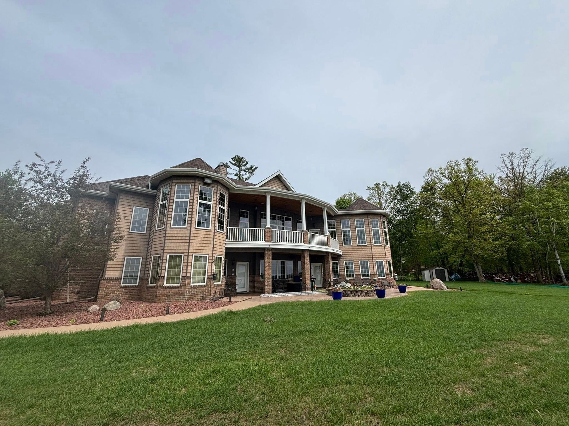 A multi-story beige house with rounded towers and a stone foundation, viewed from a grassy lawn under a cloudy sky.