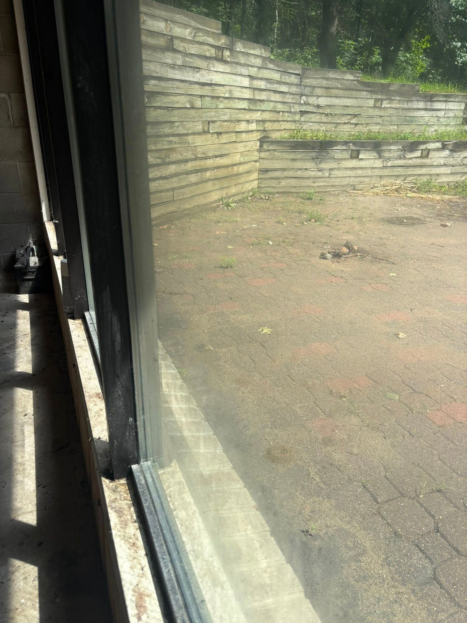 Close-up of a window frame overlooking a stone retaining wall and a paved patio area.