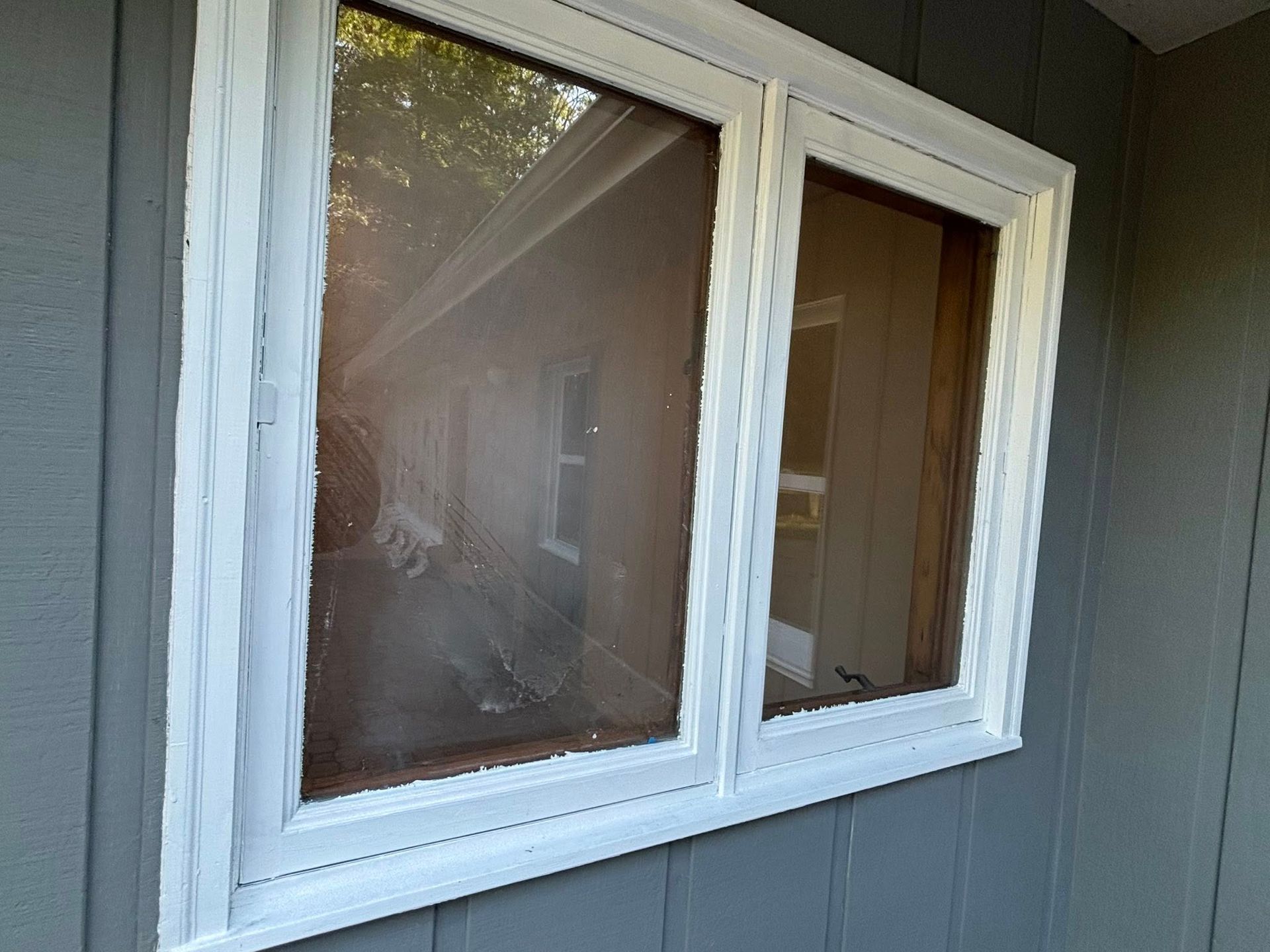 A white-framed window with reflective glass set into gray vertical wood siding on a house exterior.