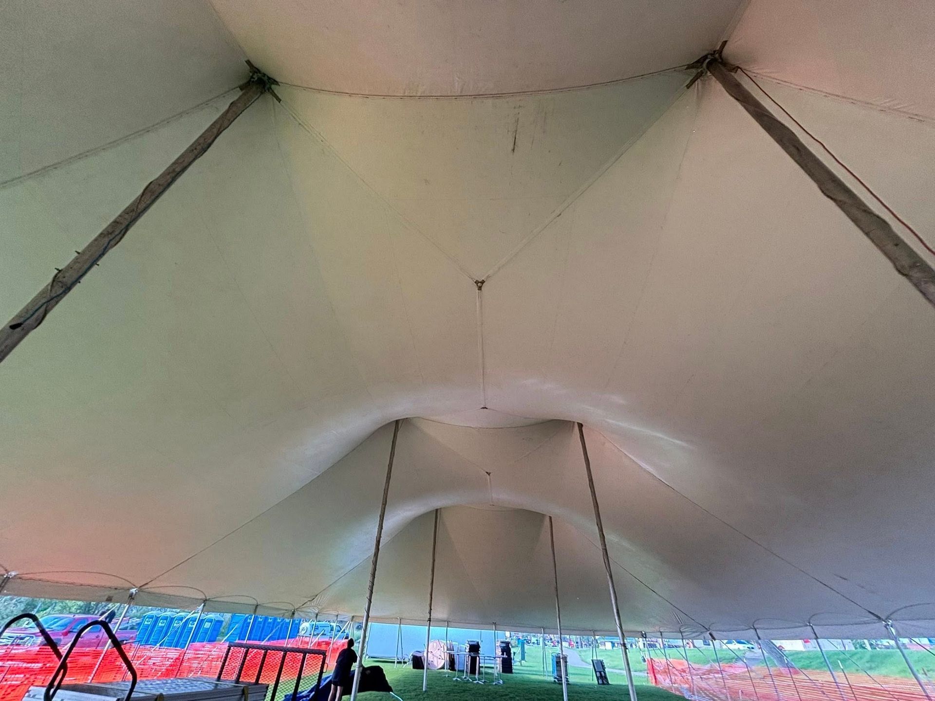Interior view of a large white event tent featuring multiple center poles and draped fabric ceiling.