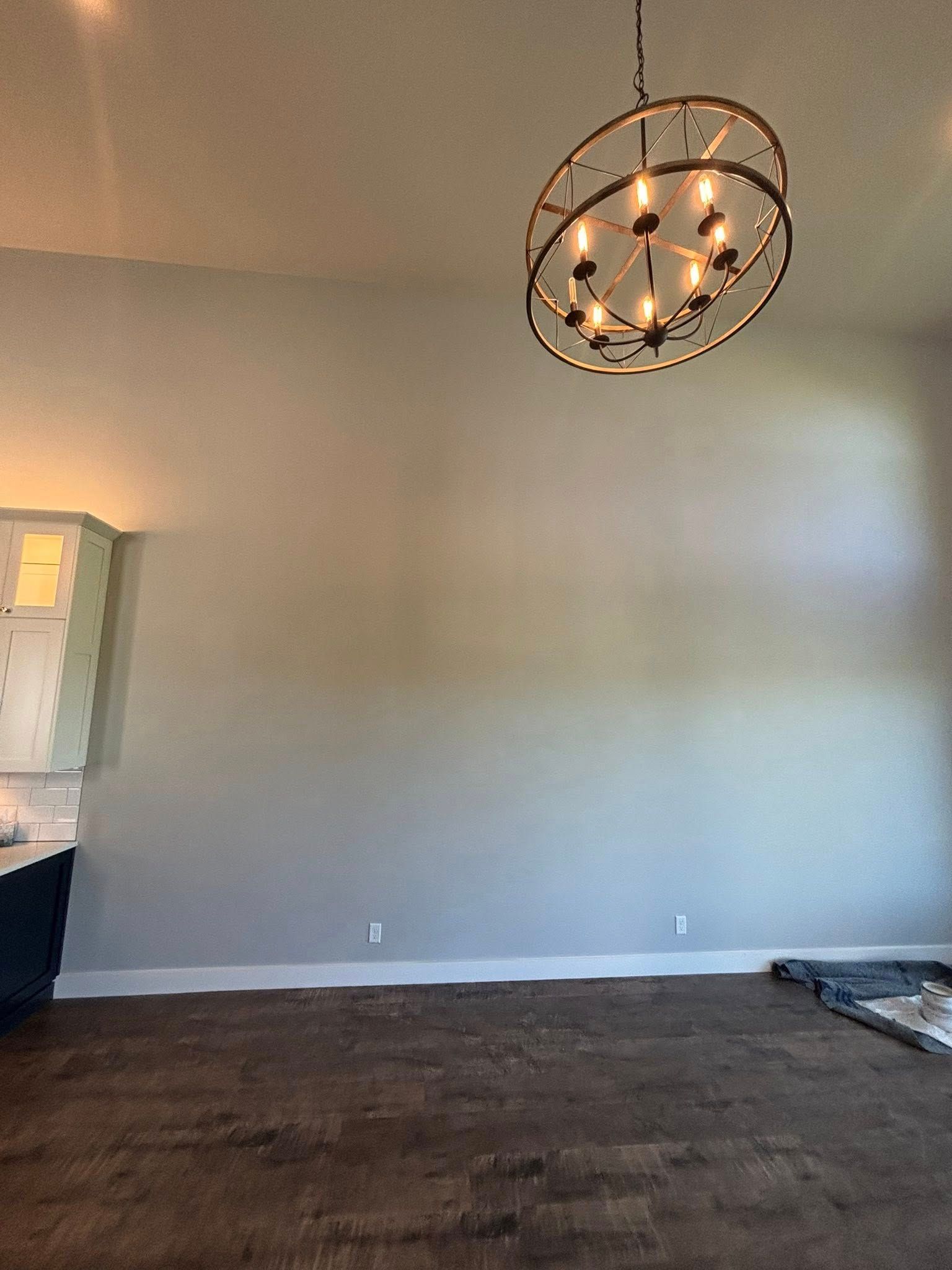 An interior view of a room with light gray walls, dark wood flooring, and a large circular chandelier overhead.