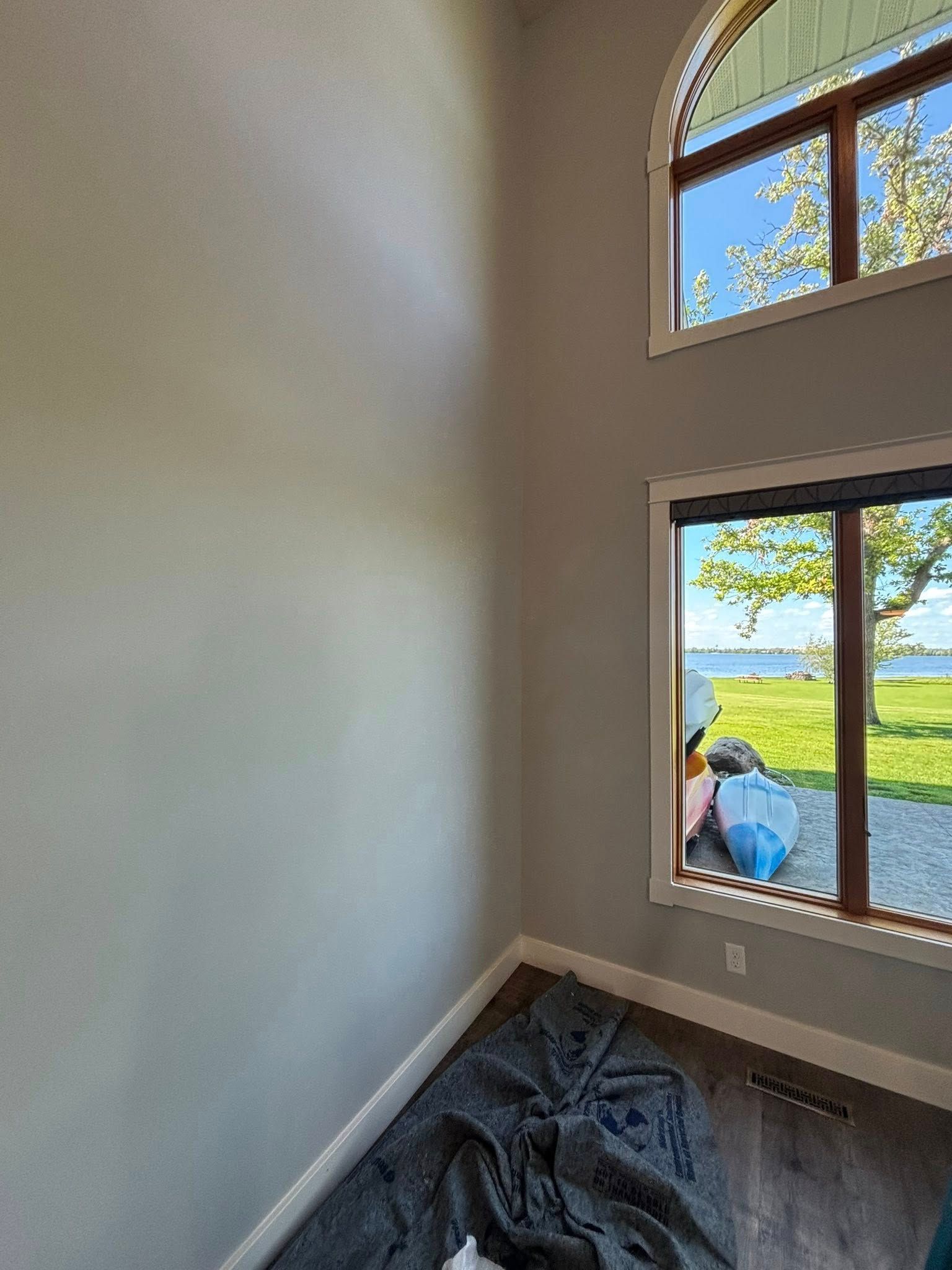 A tall, grey-painted interior wall with two windows overlooking a bright green lawn, trees, and water.
