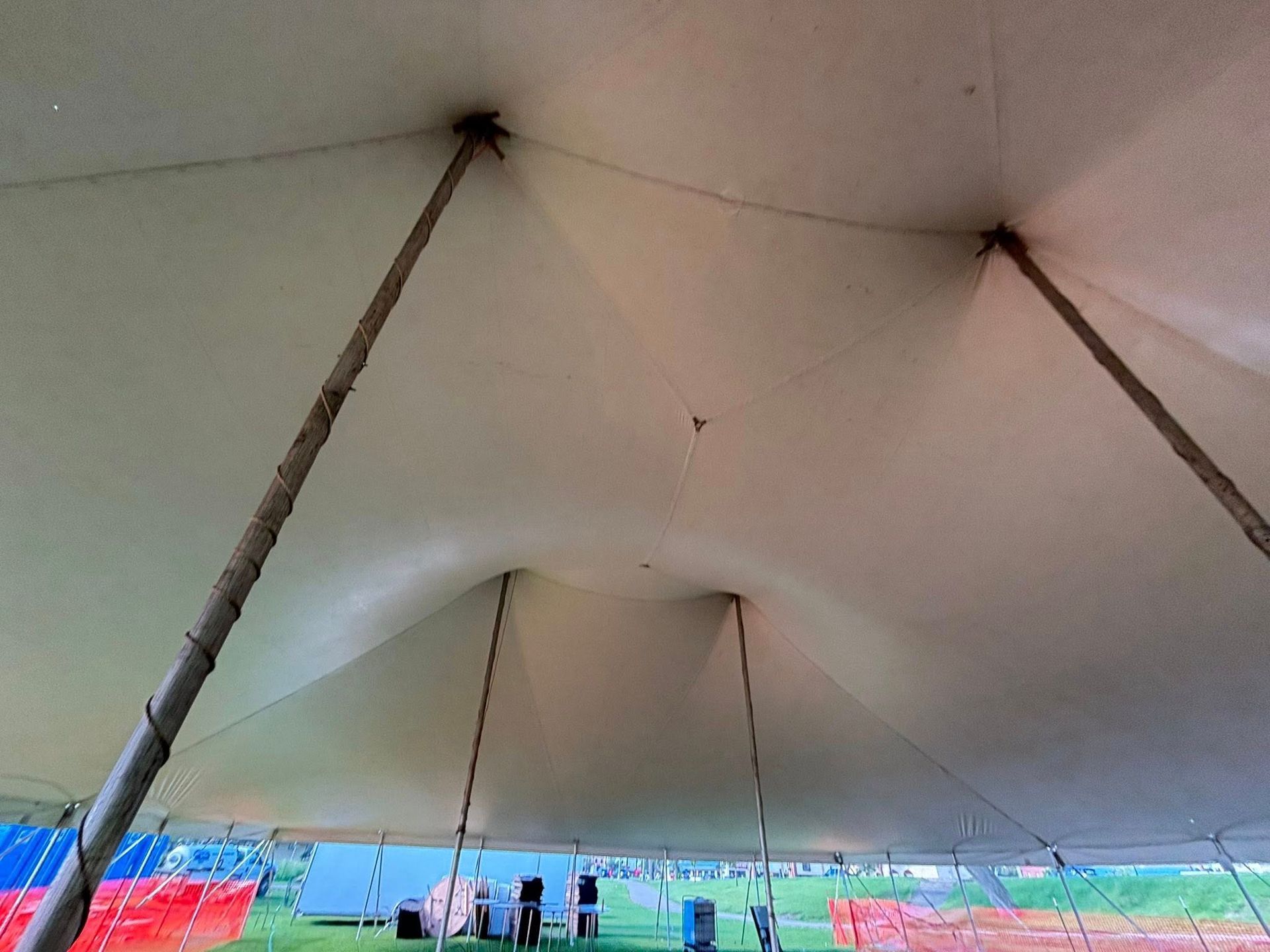 The interior view of a large white marquee tent, showing the fabric ceiling stretched over several supporting wooden poles.