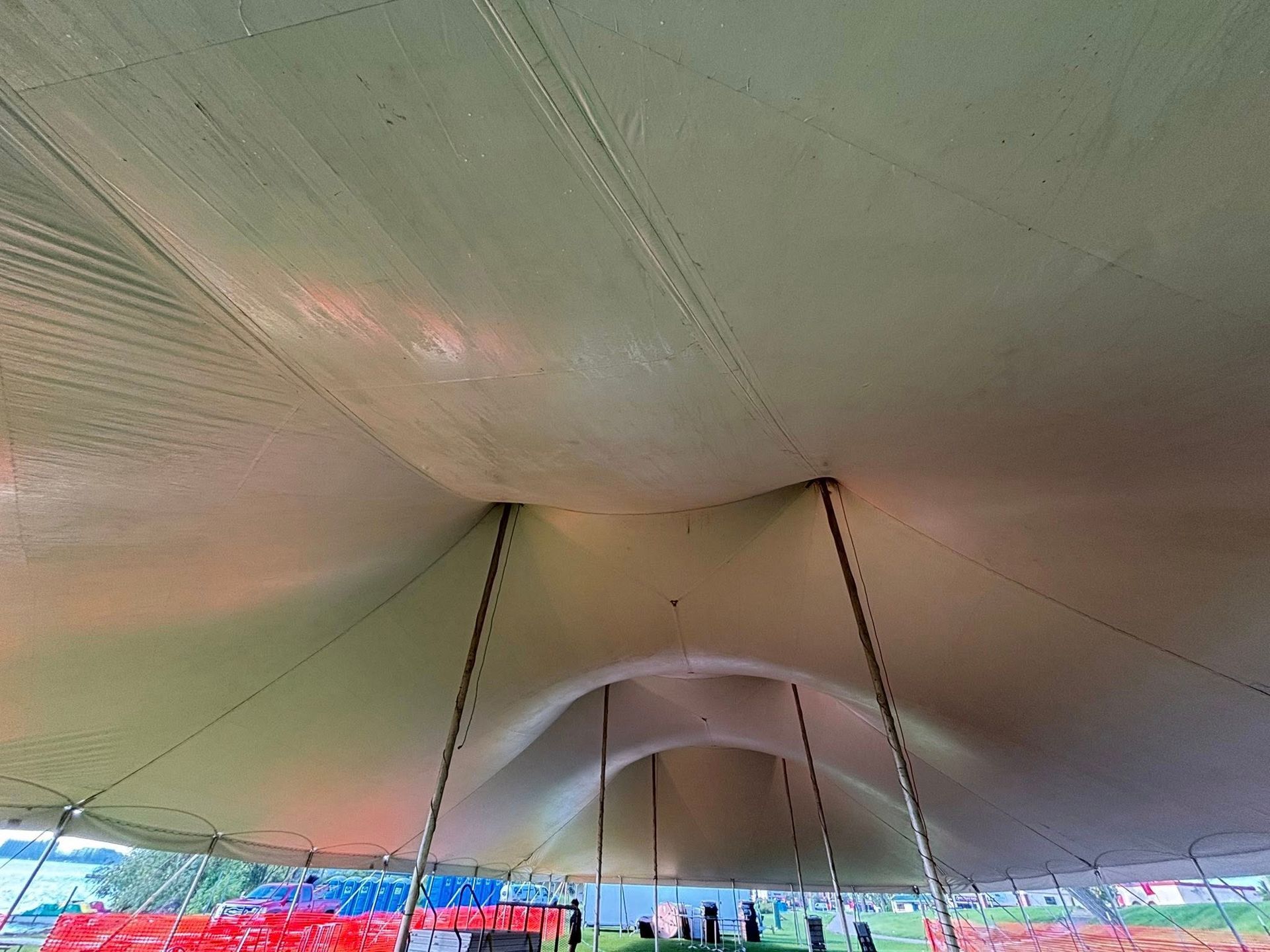 The interior view looking up at the canvas ceiling and support poles of a large event tent.