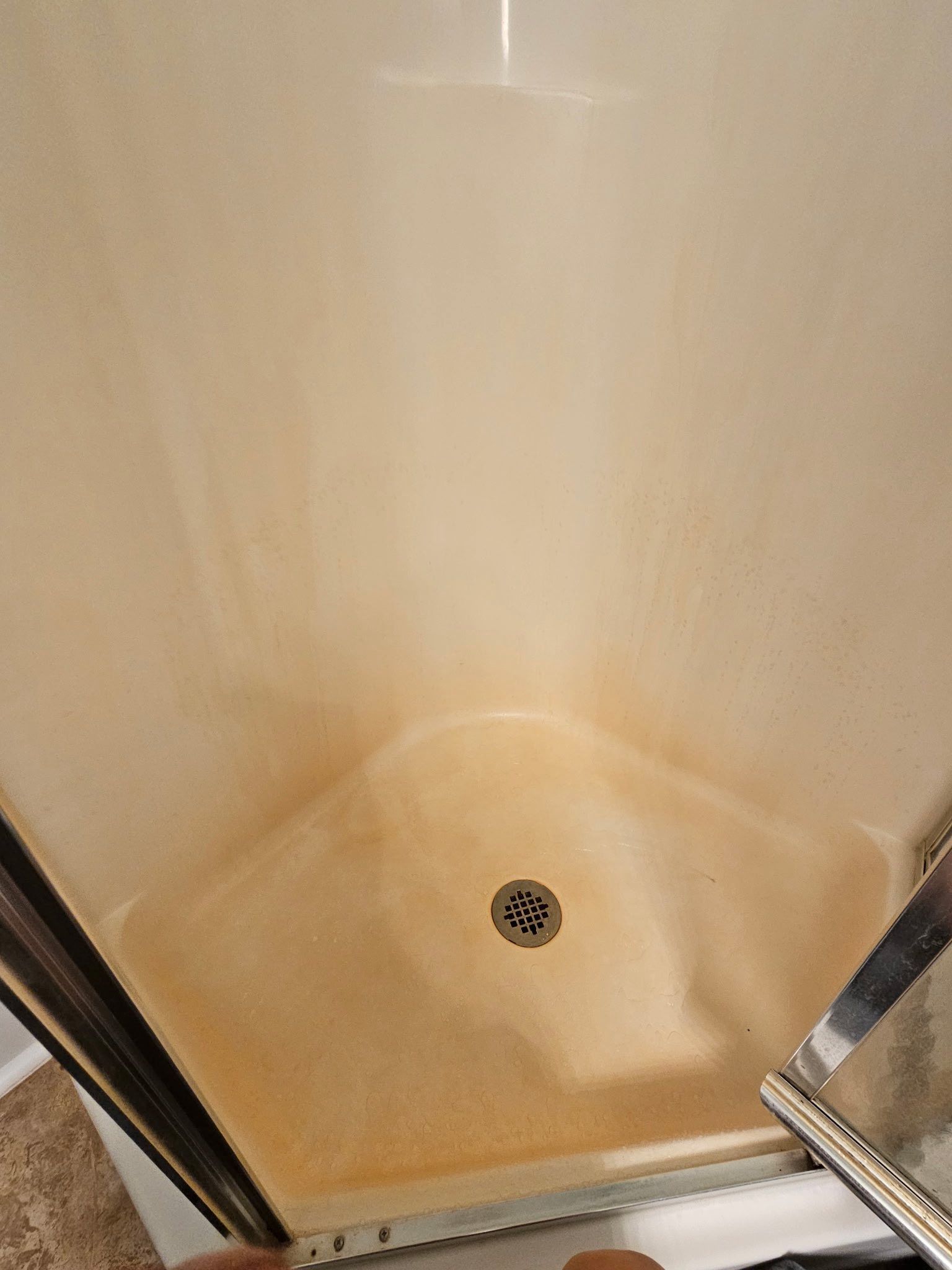 A shower stall with light-colored walls and floor heavily stained with orange-brown mineral buildup.